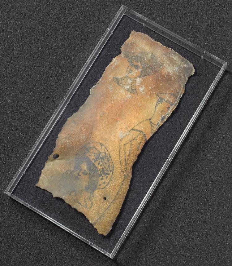 a specimen of dry-preserved skin showing three visible tattoos: two of women's heads, one the full body of a man in sailor gear, but half cut off